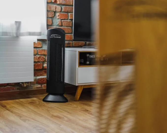 Čistička vzduchu Ionic-CARE v interiéri s tehlovou stenou a TV stolíkom, farba čierna