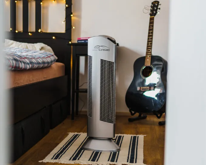 Čistička vzduchu Ionic-CARE v spálni s čiernou posteľou a gitarou opretou o stenu, farba strieborná