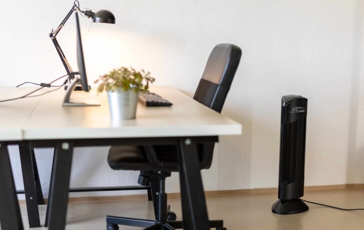 Kancelársky stôl so stoličkou a lampou, vedľa ktorého stojí čistička vzduchu Ionic-CARE v čiernej farbe