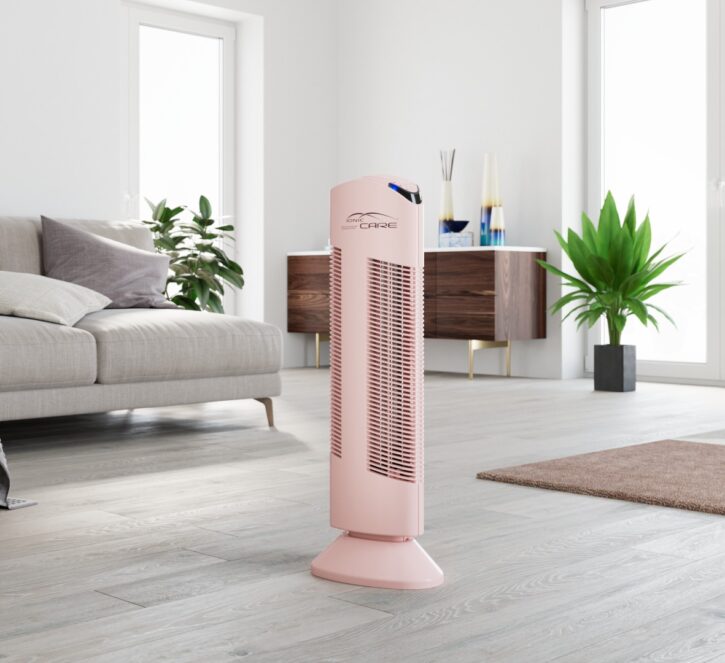 Čistička vzduchu Ionic-CARE v ružovej farbe, v obývacej izbe s pohovkou, kvety v pozadí