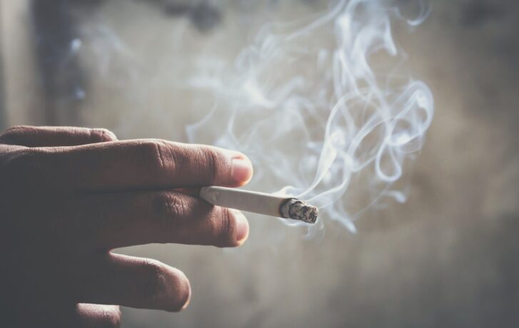 Zapálená dymiaca cigareta v ruke.