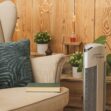 Čistička vzduchu Ionic-CARE stříbrná u sedačky s polštářem a květinami